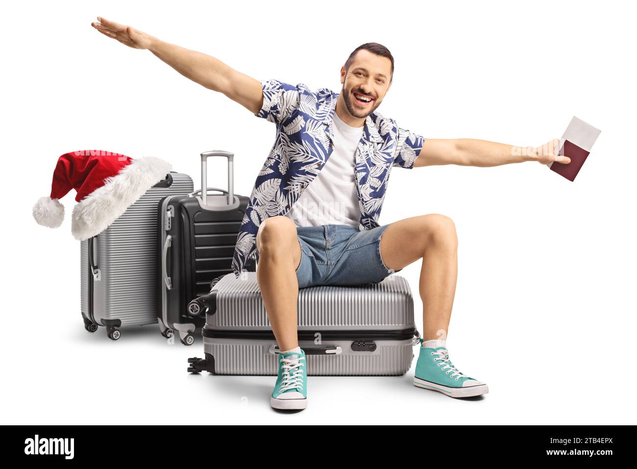 Happy male tourist going on a christmas trip, sitting on a suitcase and spreading arms to fly isolated on white background Stock Photo