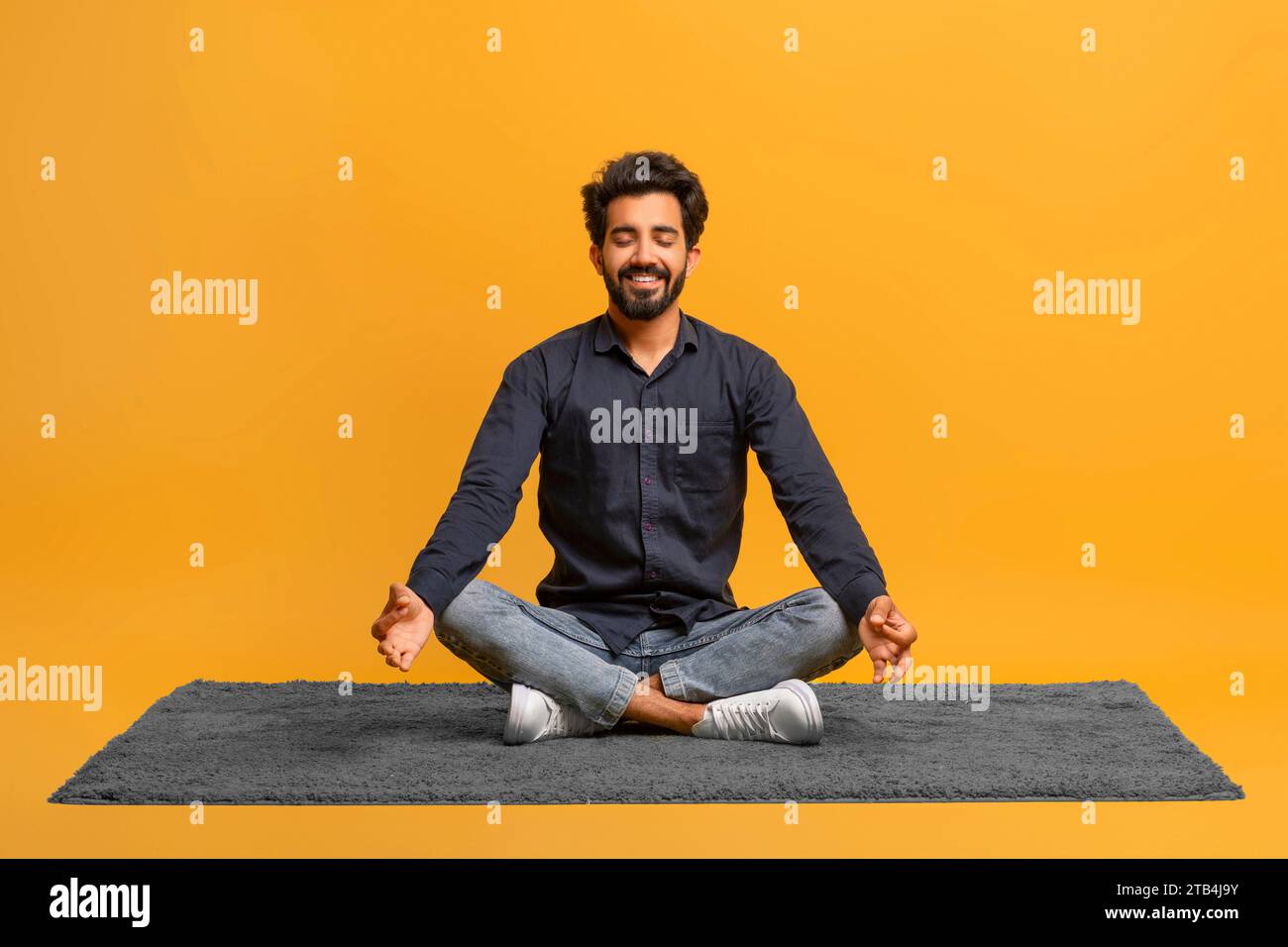 Relaxed young indian man in casual clothes meditating alone, sitting ...