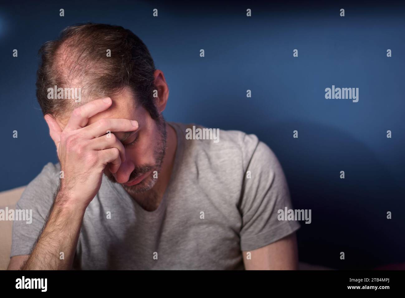 Young caucasian 30 year old man with short beard holding his head. Concept of depression, loss and grief. Adult person expressing stress and anxiety. Stock Photo