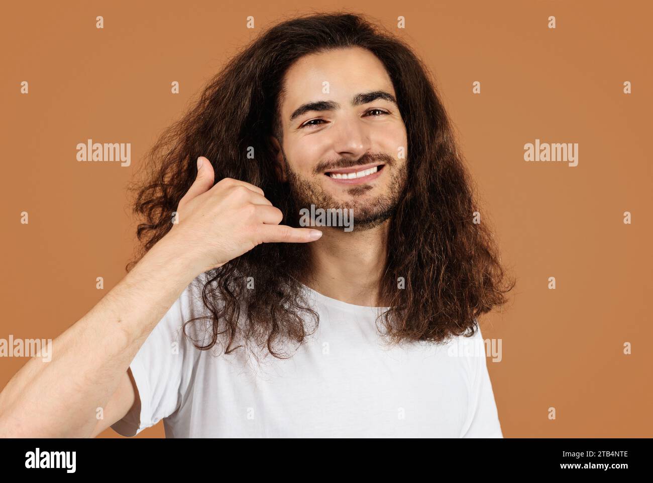 man with curly hair gesturing call me playfully, beige background Stock Photo