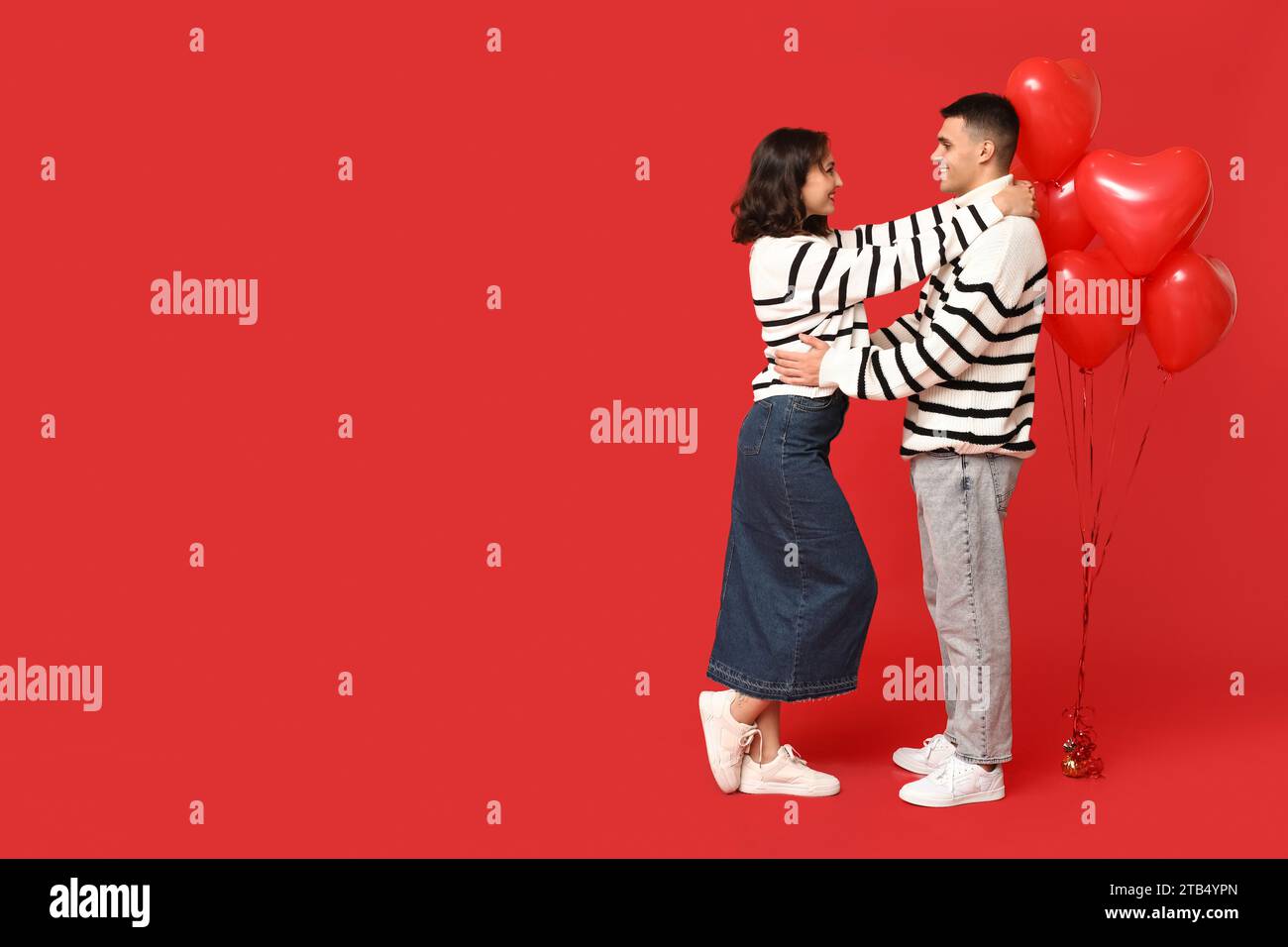 Loving young couple with heart-shaped balloons on red background ...