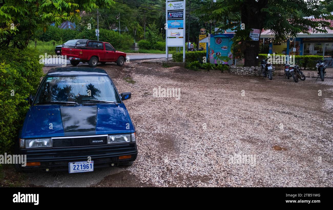 Blue Nissan and Red Toyota Pickup truck parked in Samara, Costa Rica on a dirt and gravel parking lot by the side of the main road Stock Photo