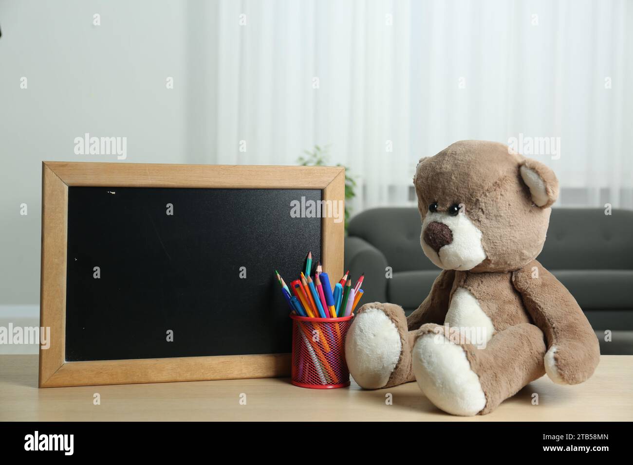 Teddy bear, small blackboard, pencils and pens in holder on wooden