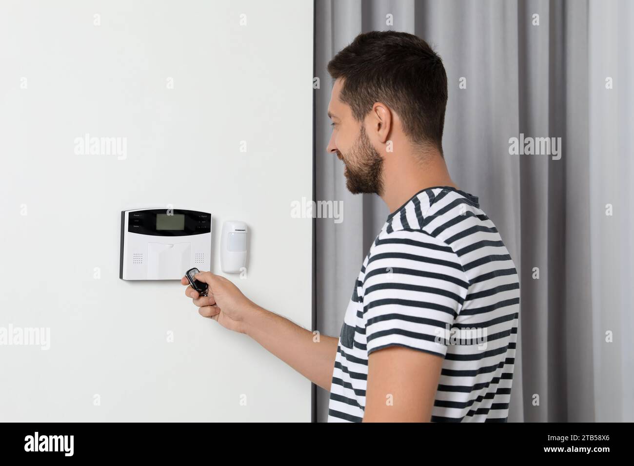 Home security system. Man using alarm key fob indoors Stock Photo
