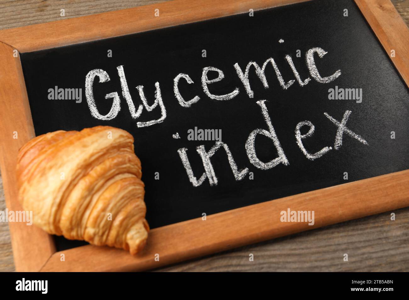 Small chalkboard with words Glycemic Index and croissant on wooden table, closeup Stock Photo