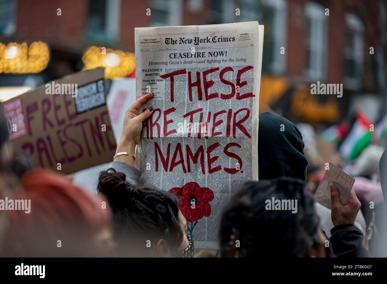 BROOKLYN, NEW YORK - DECEMBER 4: A pro-Palestine protester holds up a fabricated newspaers with the actual names of the dead while marching through the Williamsburg section of Brooklyn demanding a permanent ceasefire between Israel and Hamas on December 4, 2023 in New York City. Israel has launched relentless air and ground attacks in the Gaza Strip following an Oct. 7 Hamas attack, killing more than 15,000 Palestinians, including more than 6,000 children and 4,000 women, according to health authorities in the enclave. Thousands of buildings, including hospitals, mosques and churches, have bee Stock Photo