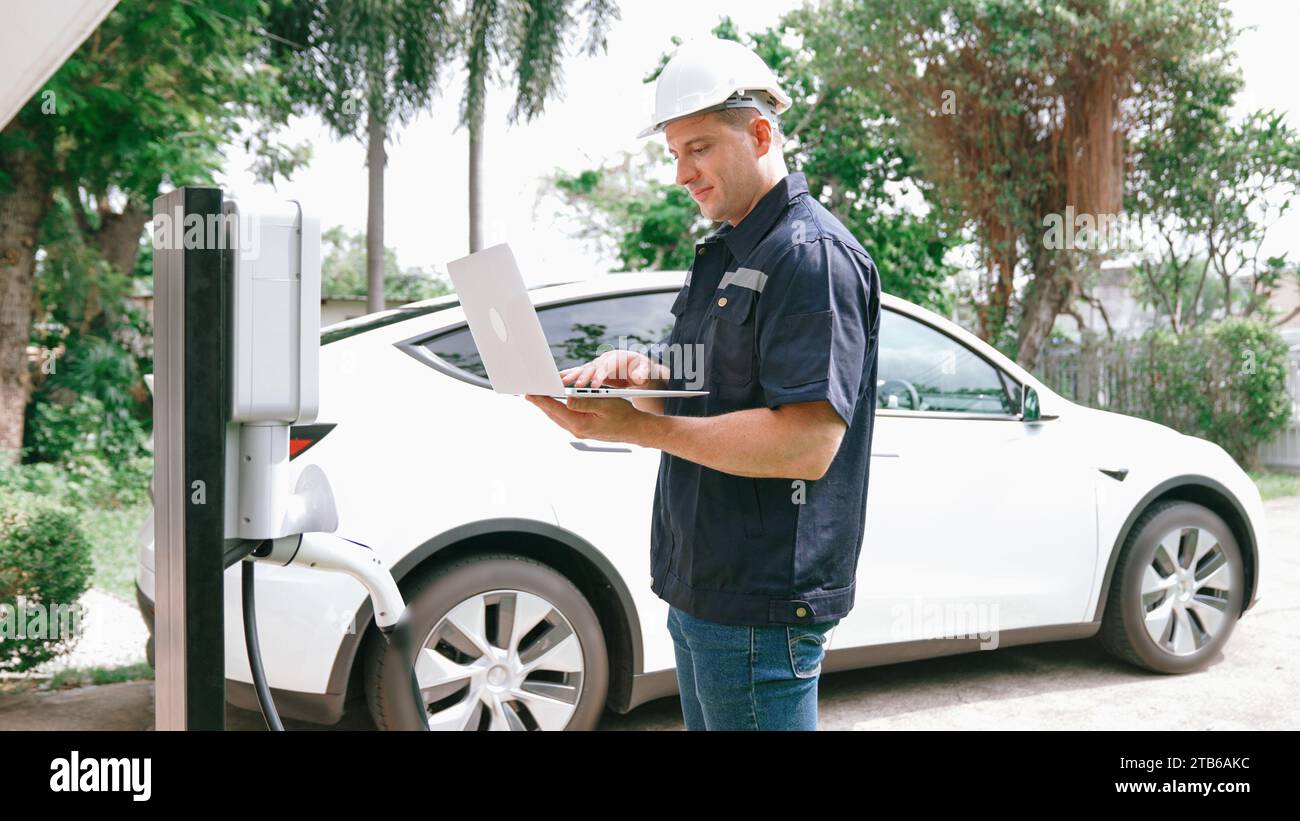 Qualified technician working on home EV charging station installation, making troubleshooting and configuration setup on charging system with laptop Stock Photo