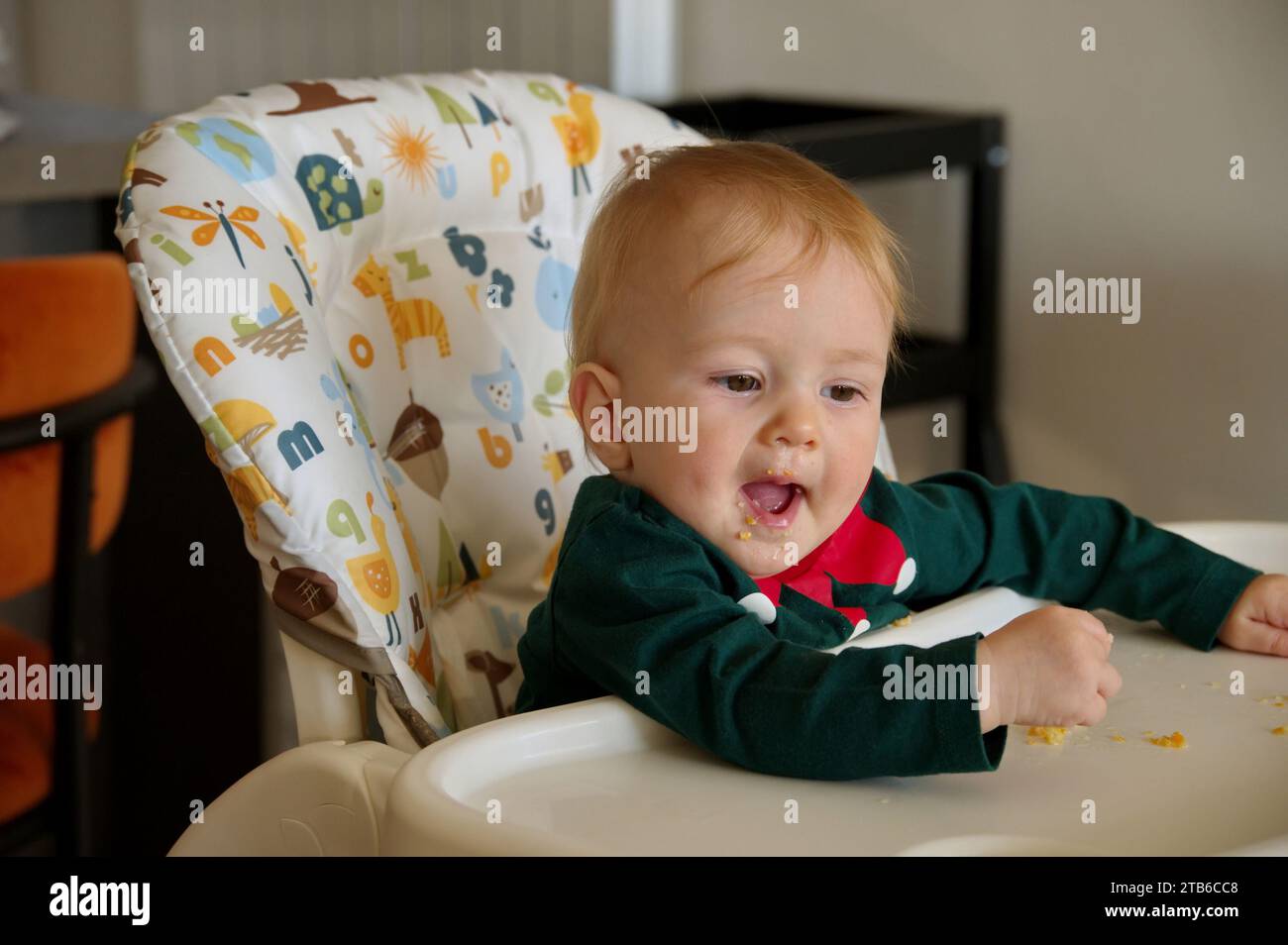 Adorable little baby girl sitting in high chair and eating Stock Photo