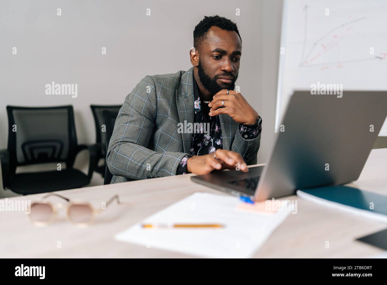 Serious black male programmer developer coding software on laptop computer typing on keyboard sitting at table in modern office room. Stock Photo