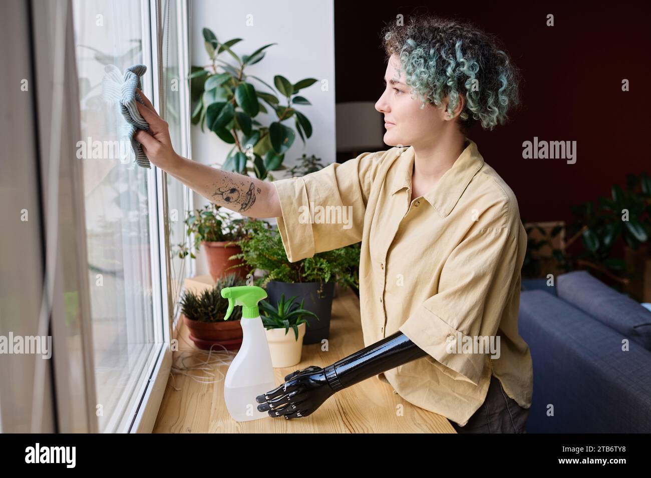 Young woman with prosthetic arm cleaning window in new apartment during move Stock Photo