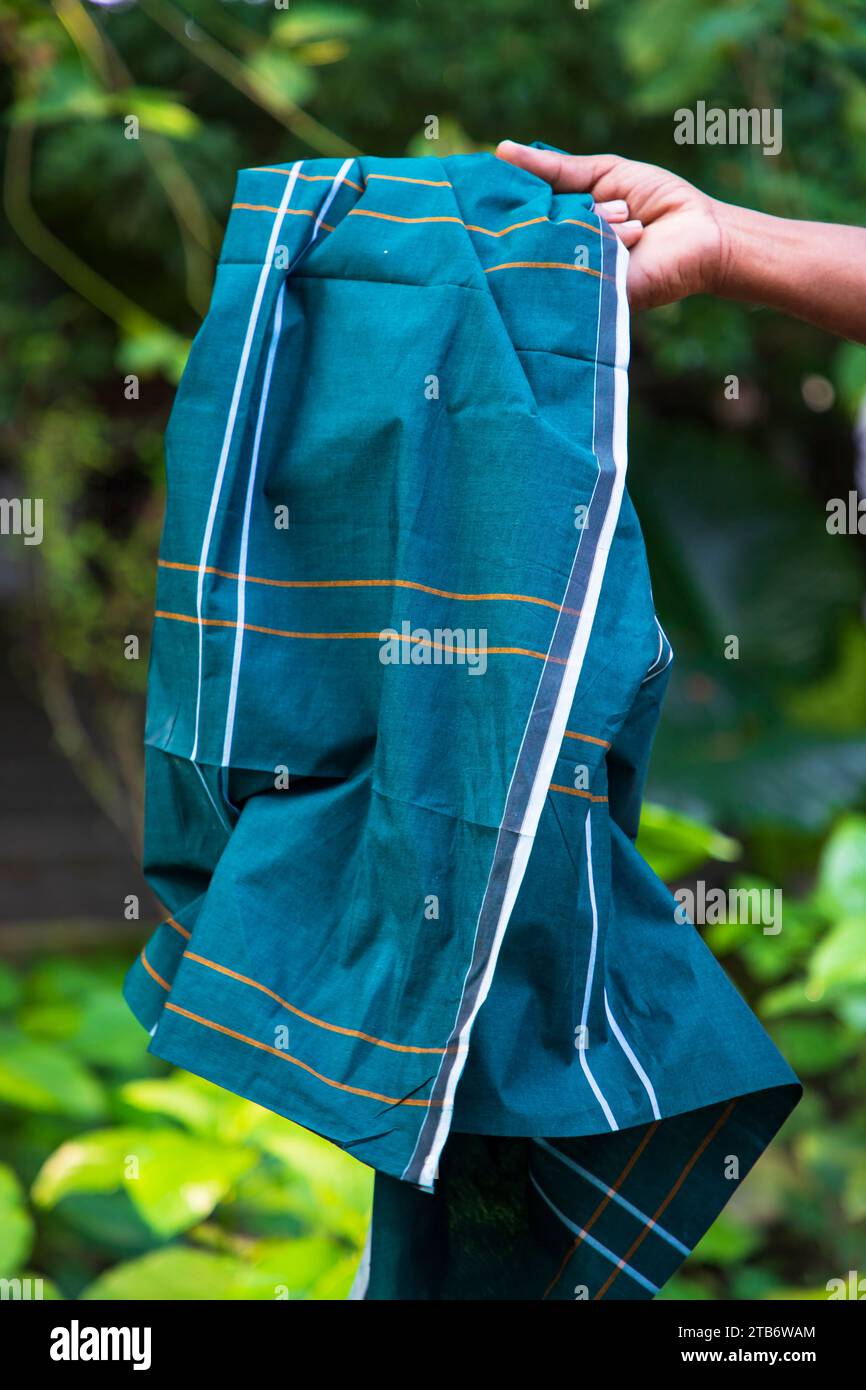 Folded Cotton Fabric Lungi hand holding with Green Blurry Background. Traditional Men's Fashion Lifestyle in Bangladesh Stock Photo