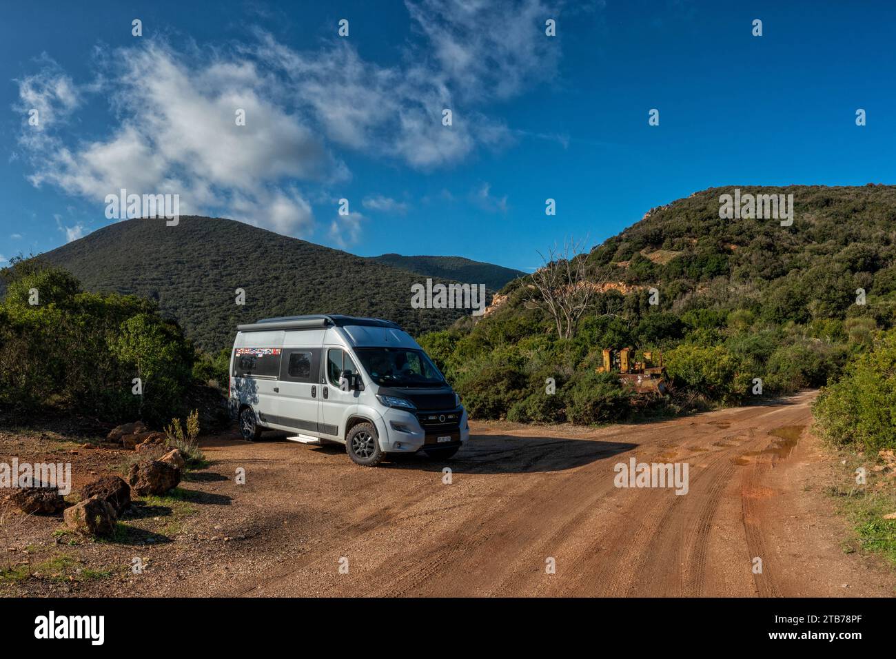 A gray campervan parked on a dirt road in the green hills of Elba under a blue sky Stock Photo