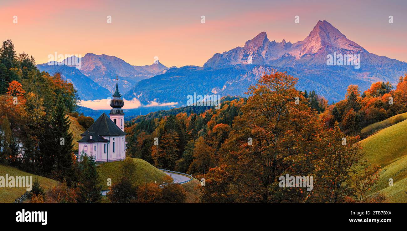 A 2:1 panorama image from an autumn sunrise with plenty of autumn colors at the Maria Gern Pilgrimage Church, with a view towards Mount Watzmann and t Stock Photo