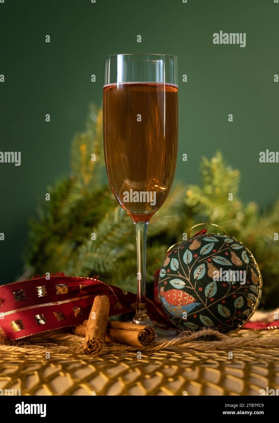 Tall glass of champagne in front of green background with Christmas tree foliage, two cinnamon sticks and a green and blue bauble Stock Photo