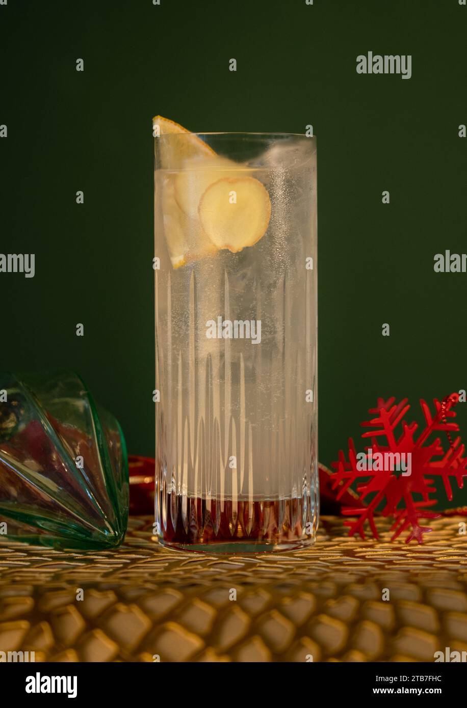 Gin and tonic in high ball glass with lemon and ice with glass bauble decorations in front of green background Stock Photo