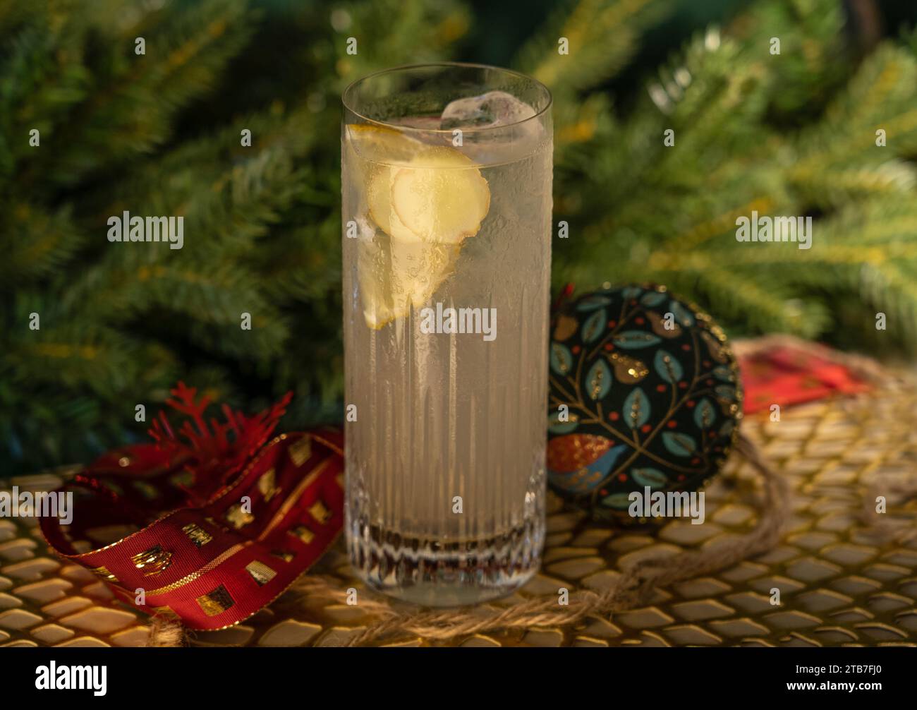 Gin and tonic in high ball glass with lemon and ice with glass bauble decorations in front of pine tree branch Stock Photo