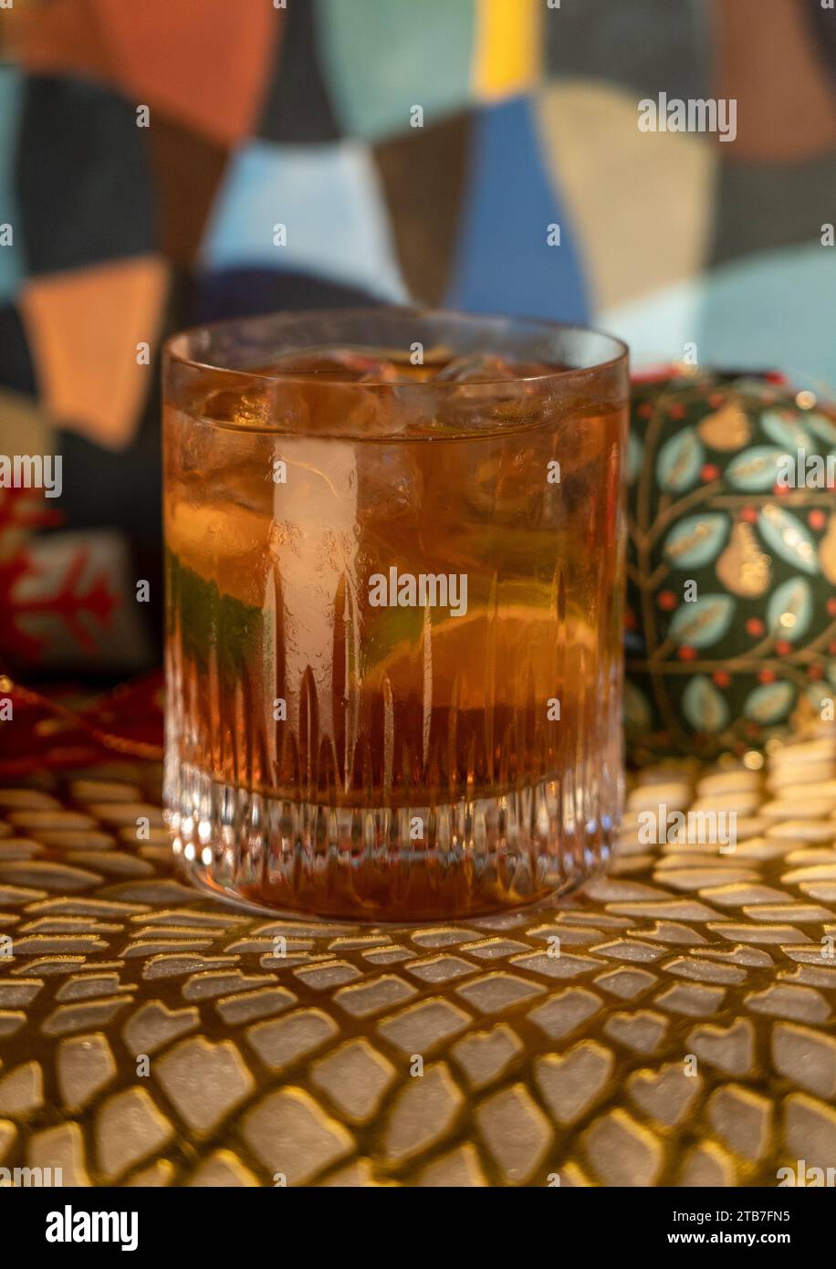 https://c8.alamy.com/comp/2TB7FN5/tequila-negroni-in-low-ball-glass-with-ice-and-lime-in-front-of-christmas-decorations-including-baubles-and-red-ribbon-on-gold-mat-2TB7FN5.jpg