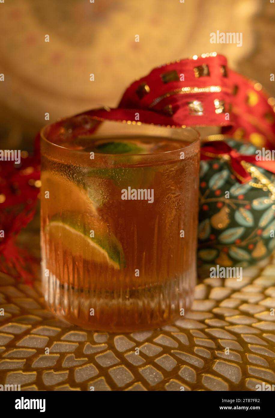 Tequila Negroni in low ball glass with ice and lime in front of Christmas decorations including baubles and red ribbon on gold mat Stock Photo