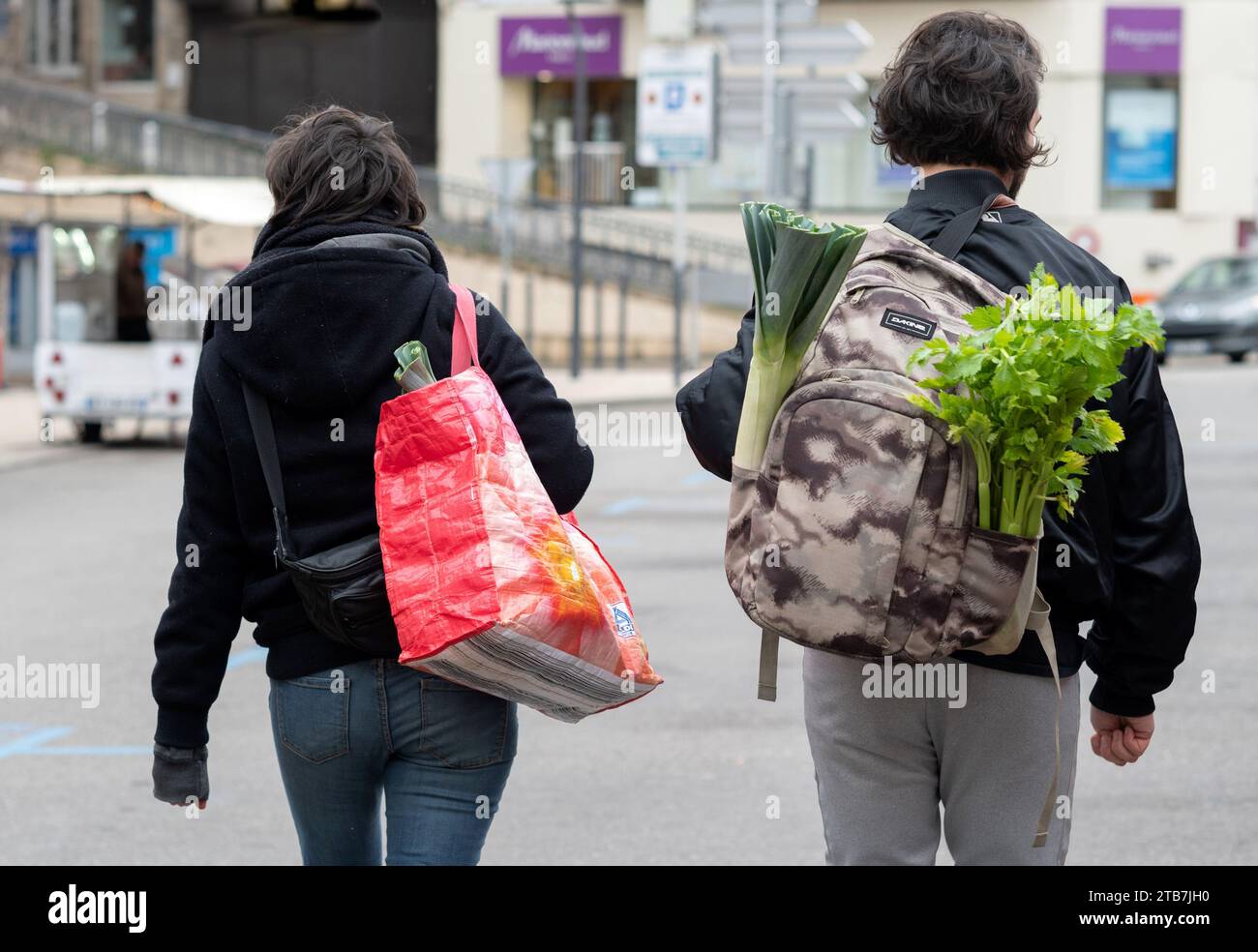 Annonay (south-eastern France): atmosphere on a winter market day. Young couple with shopping bags and vegetables sticking out of a backpack, leeks an Stock Photo