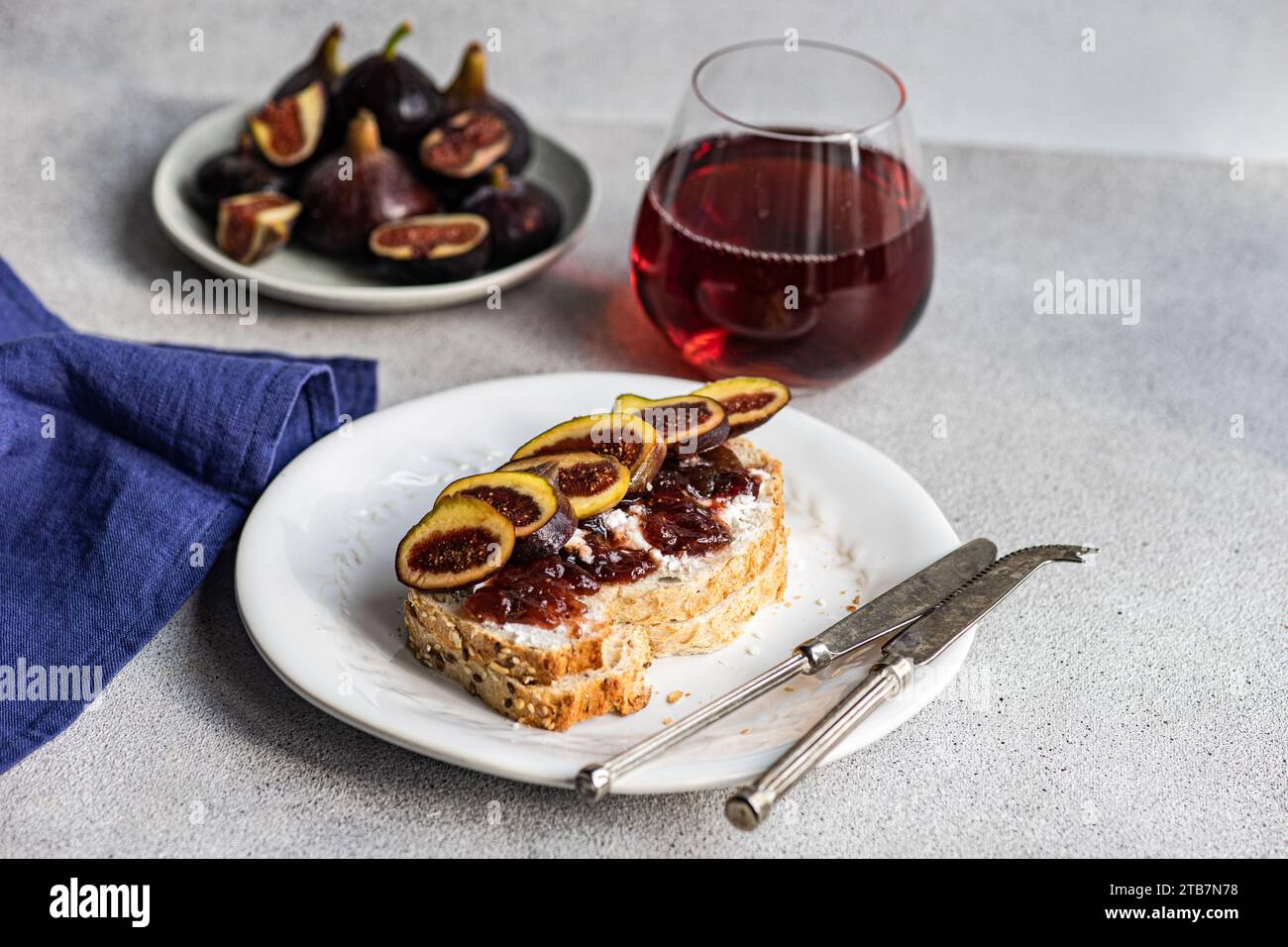 A gourmet toast topped with figs and jam, paired with a glass of red wine, presented on a white plate for a sophisticated snack. Stock Photo