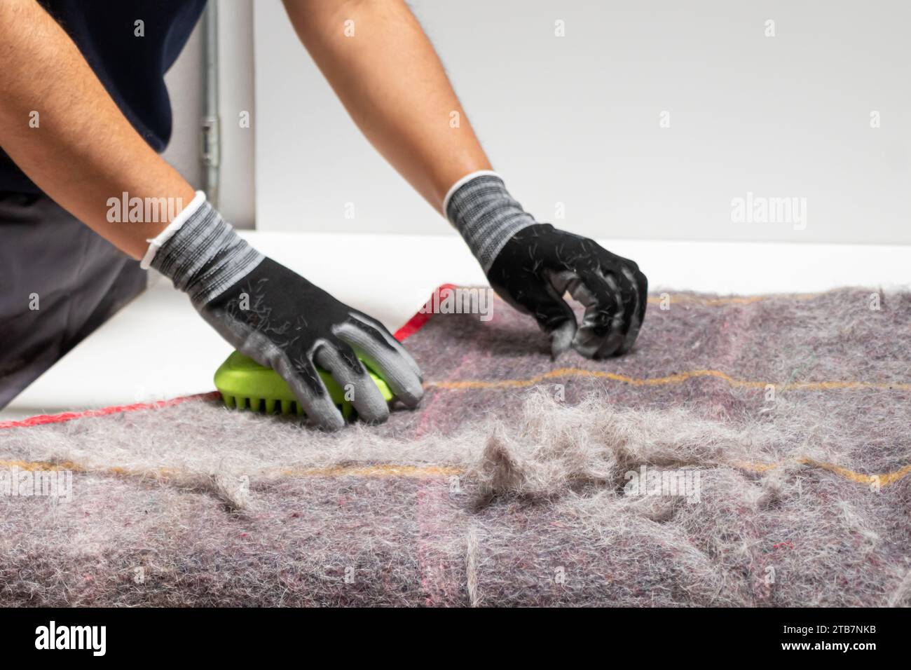Side view of cropped unrecognizable person's hands in gloves using a fur removal tool to clean a pet hair-covered blanket Stock Photo