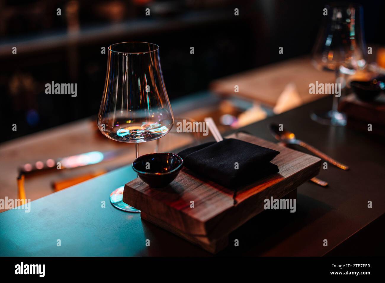 An intimate setting of a sushi restaurant with a wooden table, elegant glassware, and a stone plate awaiting delicious cuisine. Stock Photo