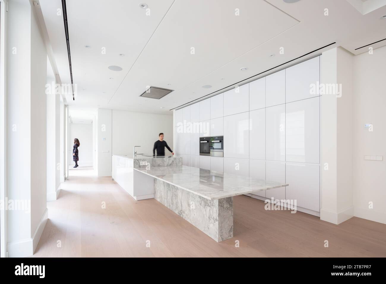 Man walking by countertop and white cabinets in spacious modern kitchen ...