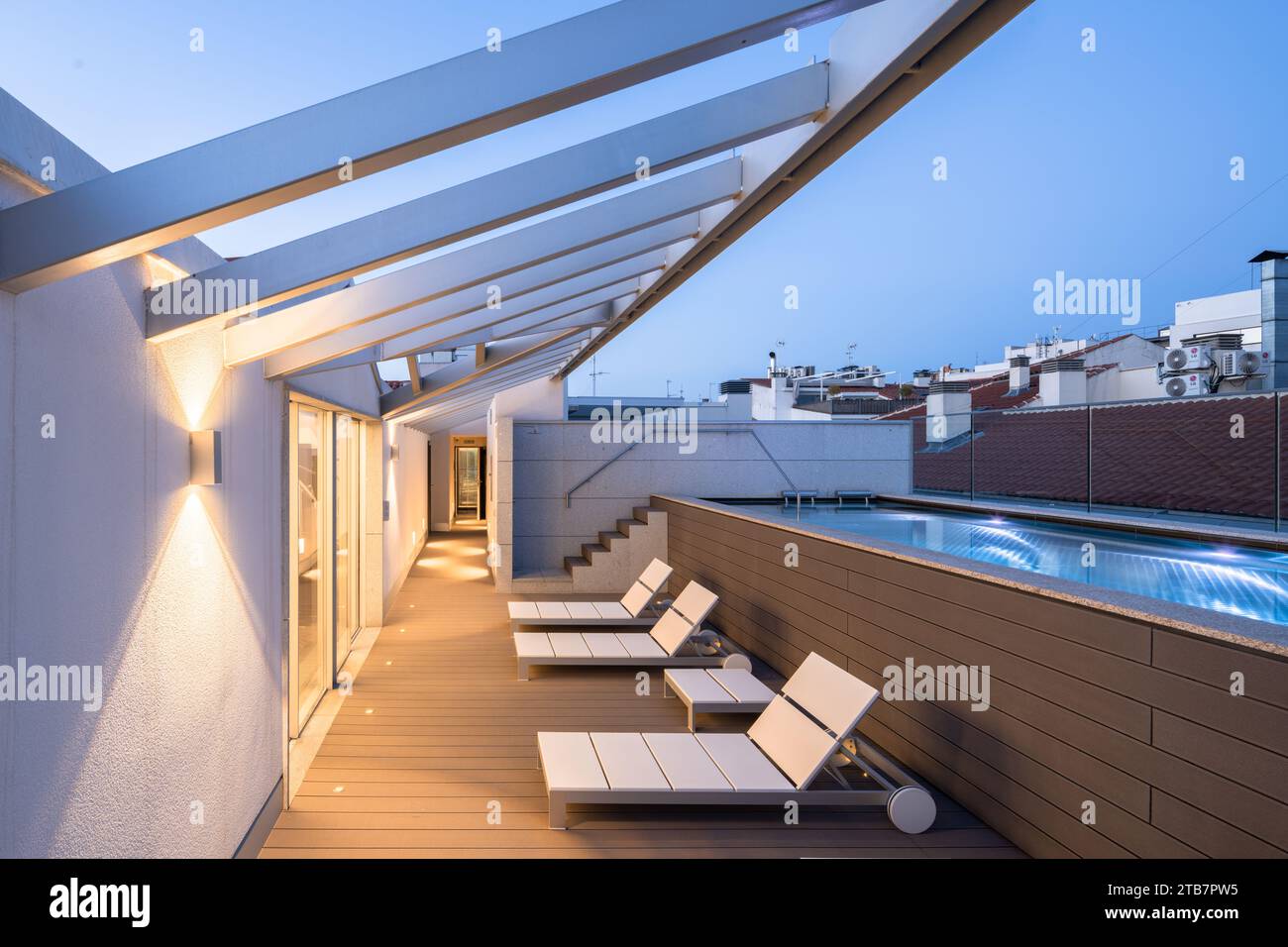 Swimming pool on rooftop terrace with empty lounge chairs under pergola ...
