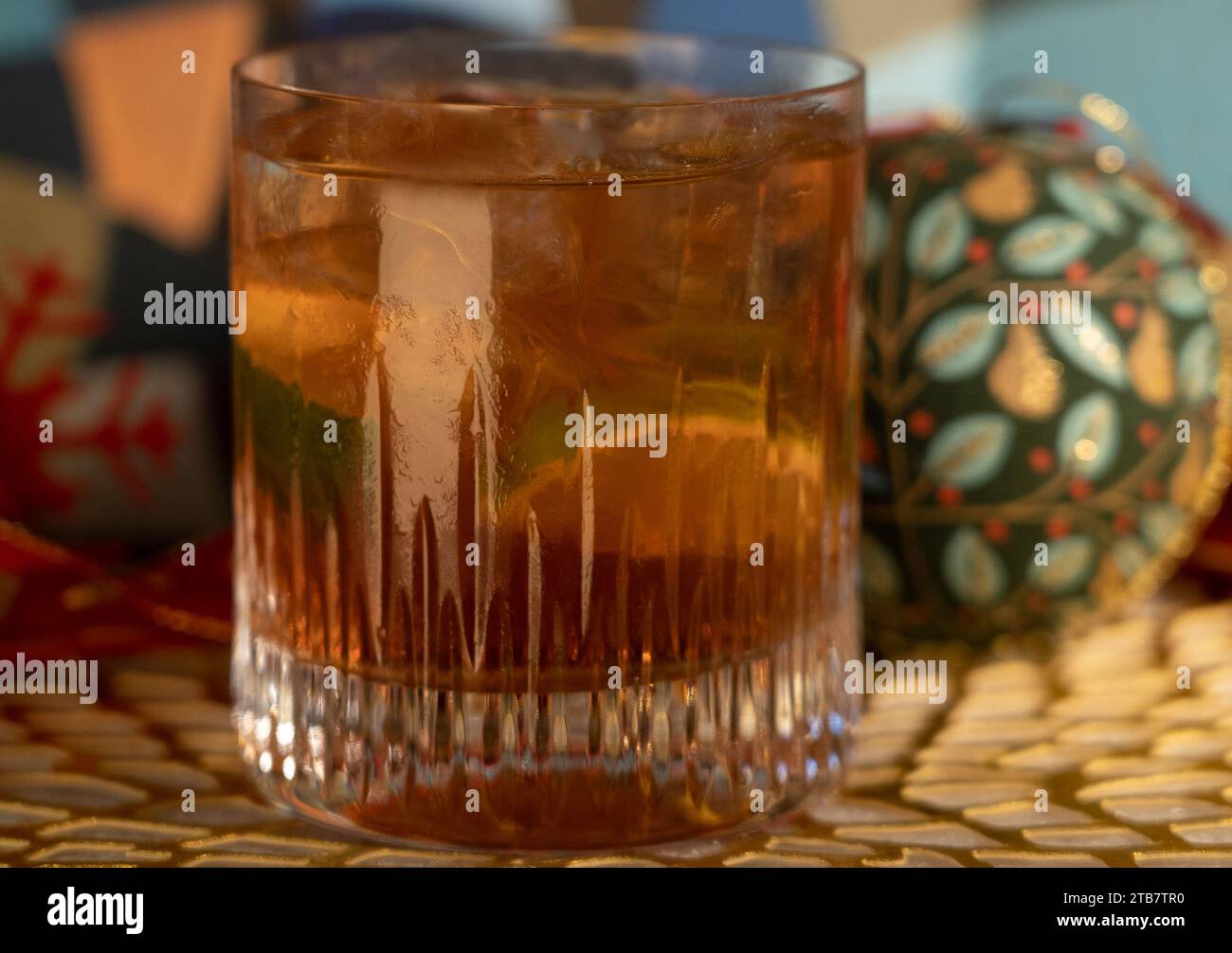 Tequila Negroni cocktail in low ball glass with ice and lime in front of Christmas decorations including baubles and red ribbon on gold mat Stock Photo