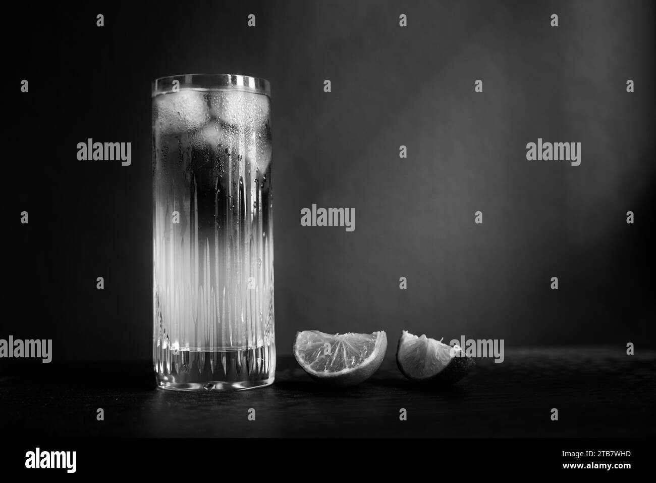 Dark and Stormy cocktail in black and white served with ice and lime on a white table cloth in front of a dappled background Stock Photo