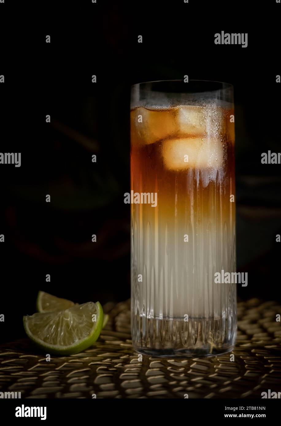 Dark and Stormy highball cocktail with ice and lime in front of green background Stock Photo