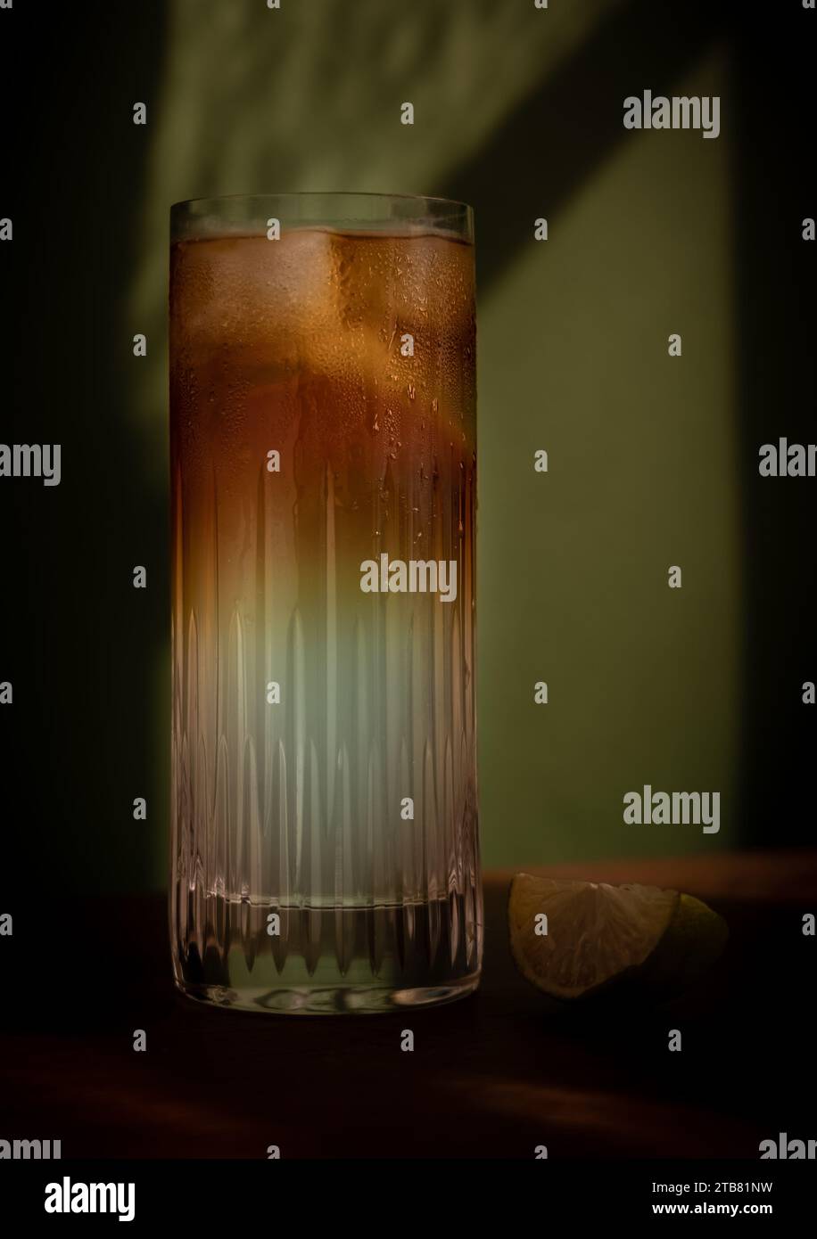 Dark and Stormy highball cocktail with ice and lime in front of green background Stock Photo