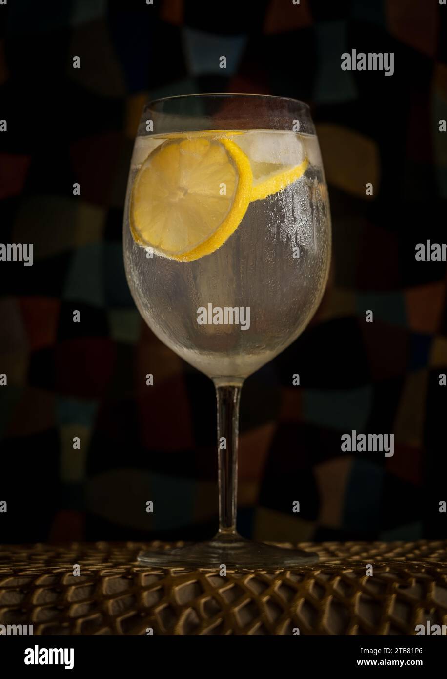 Gin and Tonic highball cocktail with ice and lemon in front of green