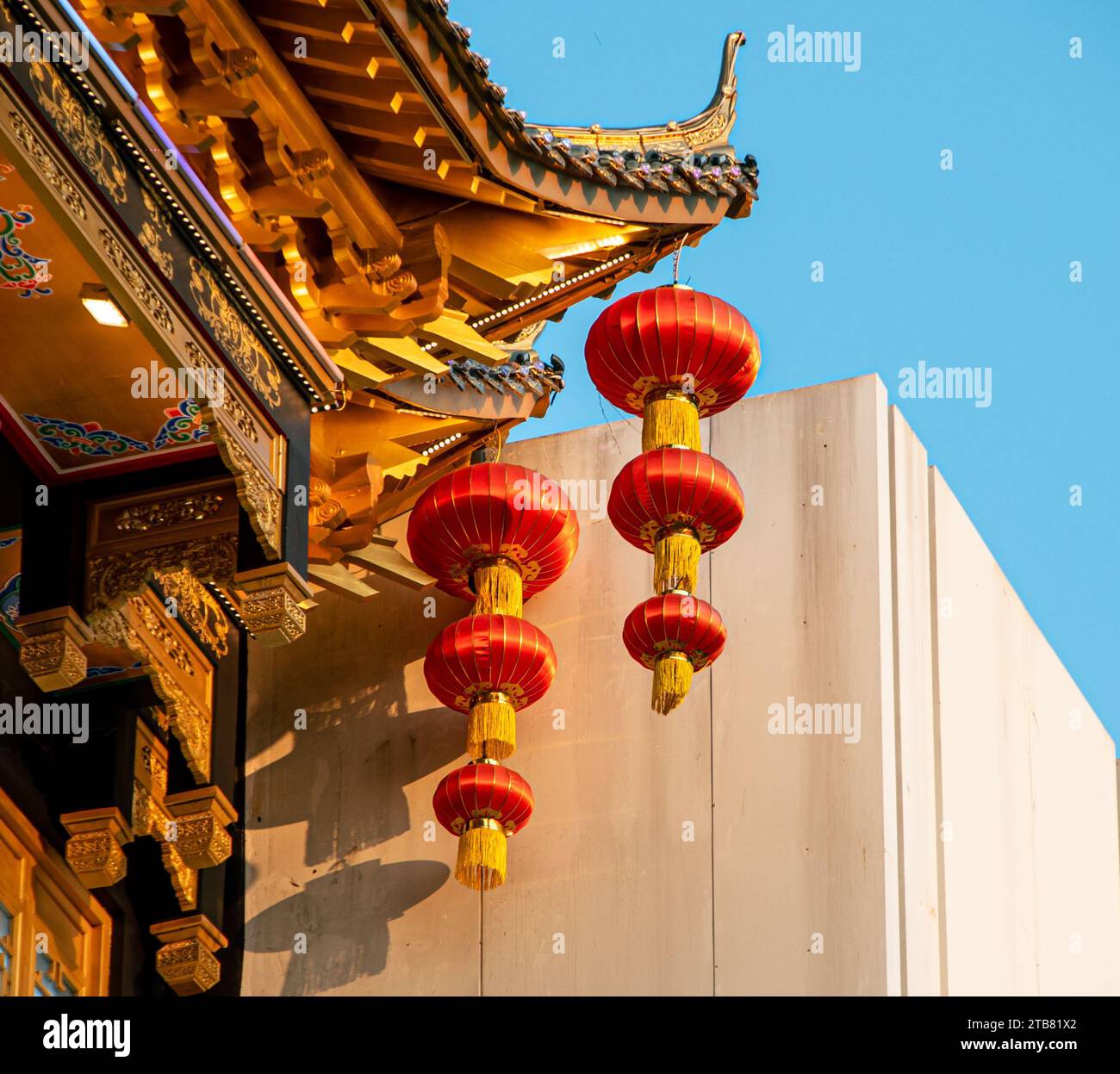 A row of vibrant red Chinese lanterns hang below the ornate eaves of a ...