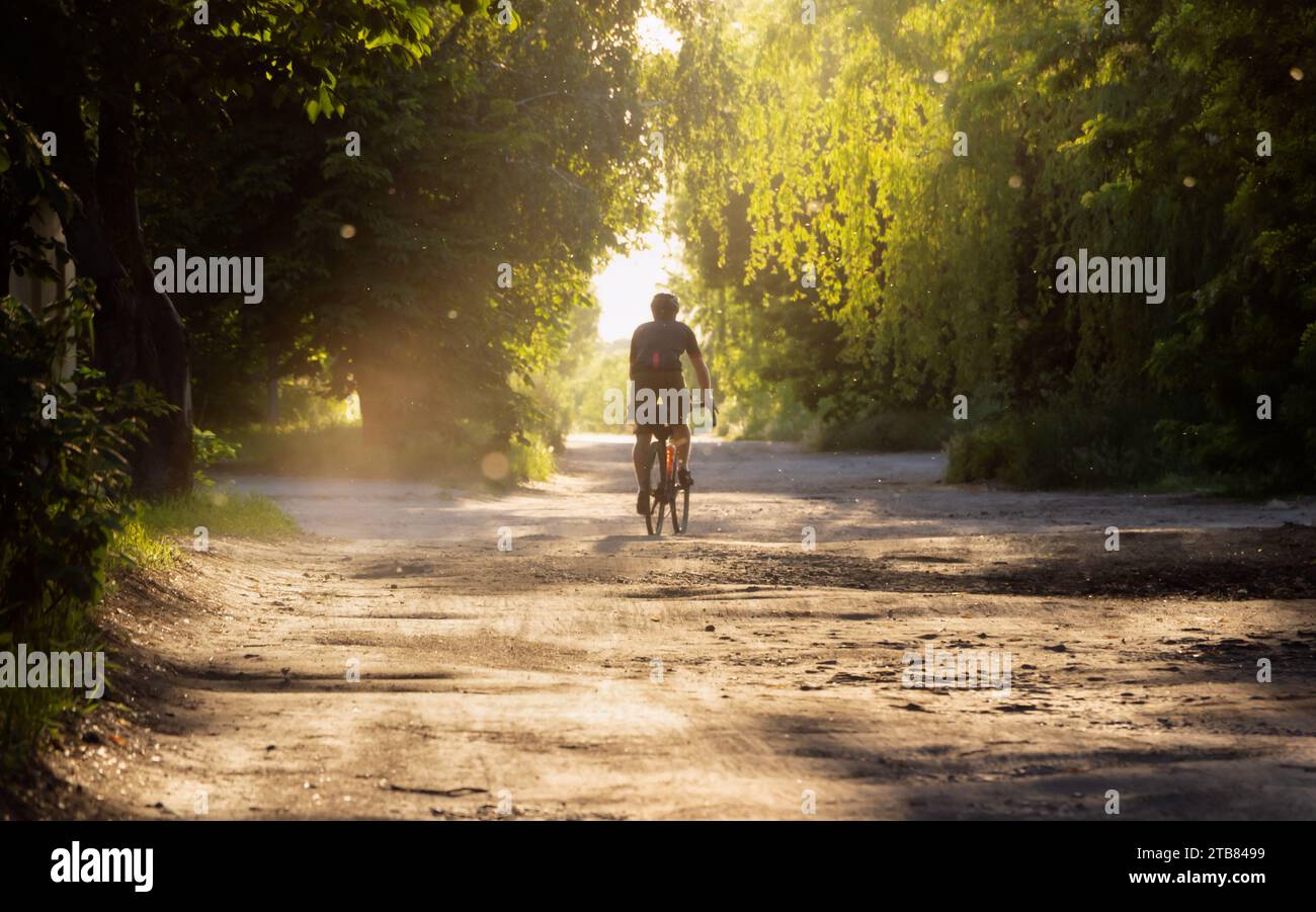 Cyclist rides bicycle on a gravel road at sunset. Soft focus. Stock Photo