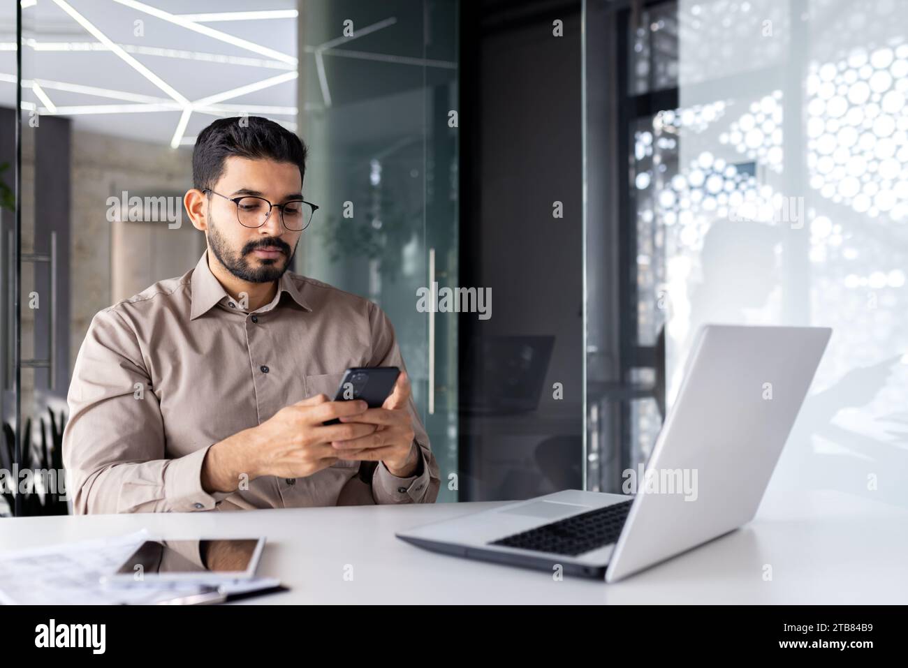 Serious concentrated businessman at the workplace inside the office, the man holds a smartphone in his hands, a worker with a laptop browses the Inter Stock Photo