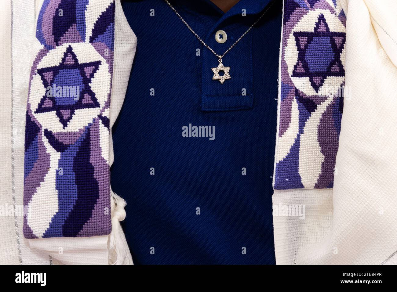 Detail of a Jewish man wearing a tallit or prayer shawl decorated with Jewish stars and a necklace with a gold Magen David pendant. Stock Photo