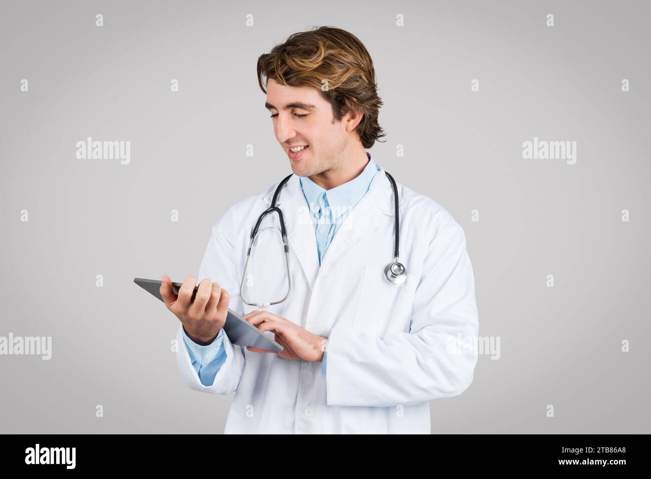 Focused male doctor using digital tablet on grey background Stock Photo