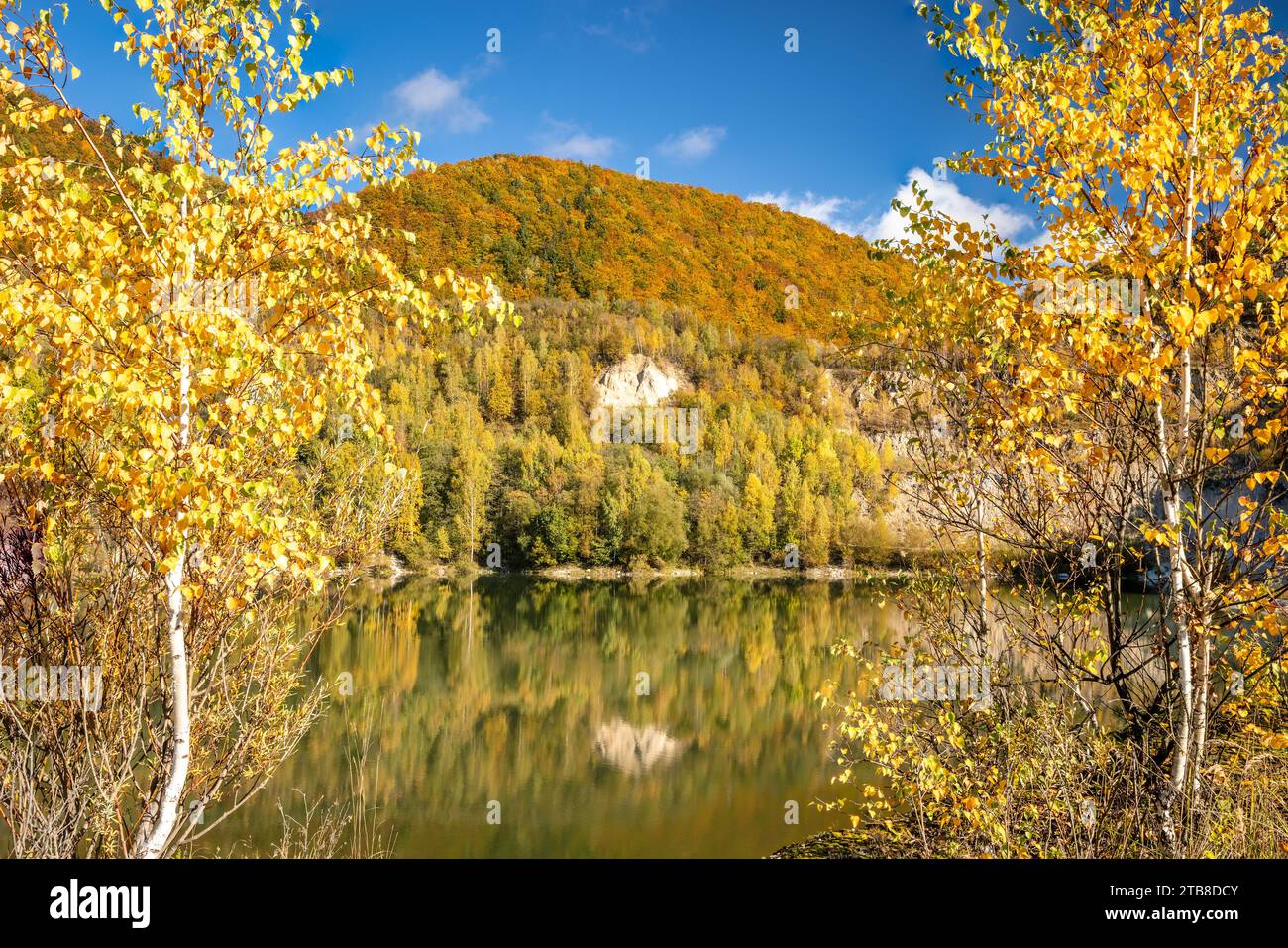 Autumn landscape with a lake by the hills covered with colorful forests. Flooded quarry near the village Sutovo in Slovakia, Europe. Stock Photo