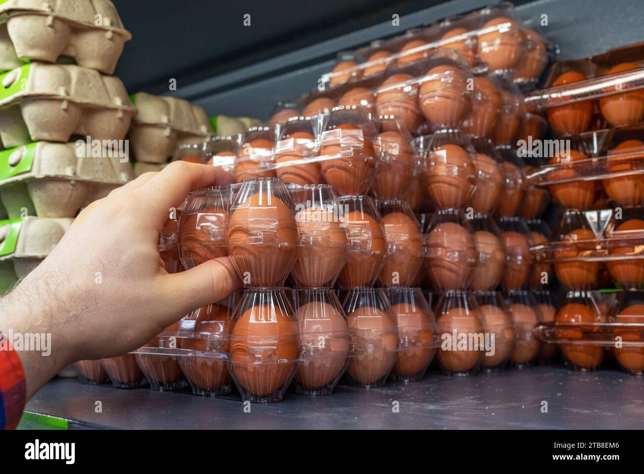 Chicken eggs on the store shelf. A customer takes a packaging of chicken eggs from a supermarket fridge. Containers of chicken eggs in a refrigerator Stock Photo