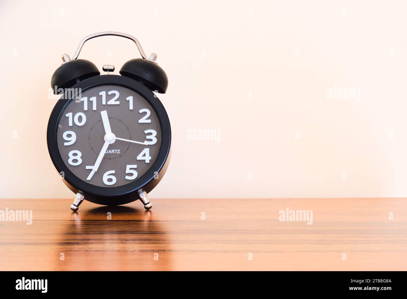 A vintage style alarm clock on a wooden table showing the time as late morning with natural daylight coming in. Copy space to the right. Stock Photo