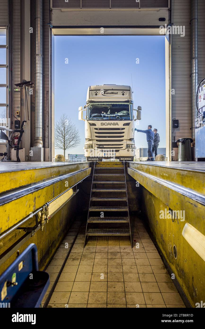 Garage, repair shop for heavy goods vehicles: interior of the workshop pit. Mechanic and Scania truck about to be positioned over the inspection pit Stock Photo