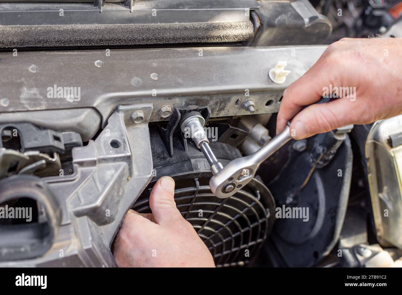 A man fixes an engine cooling fan under the radiator grill of a car ...
