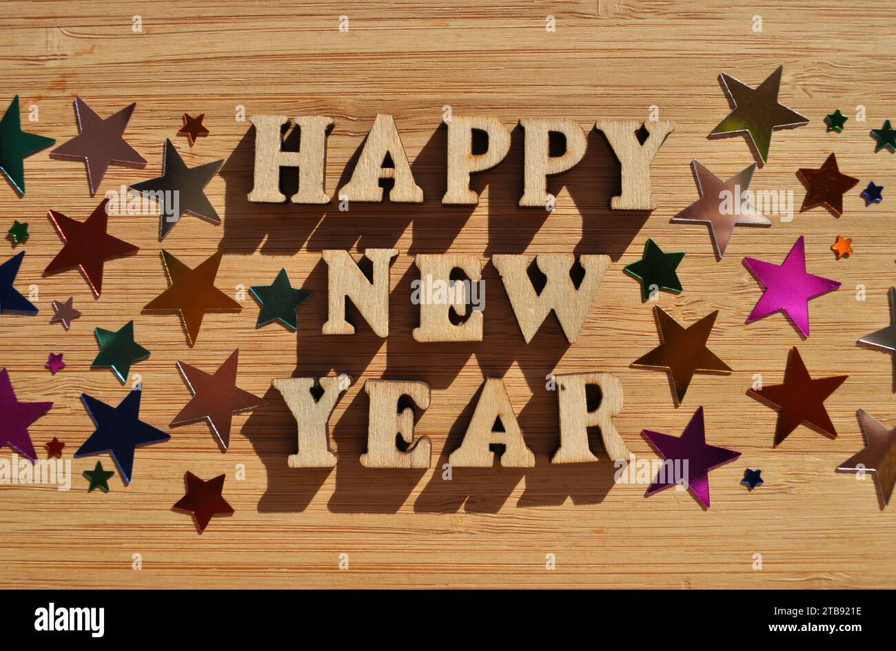 Happy New Year, words in wooden alphabet letters surrounded by random confetti stars isolated on wood background Stock Photo