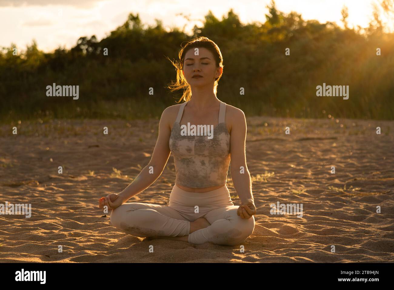 Young beautiful woman practicing yoga outdoors sitting on a beach in ...