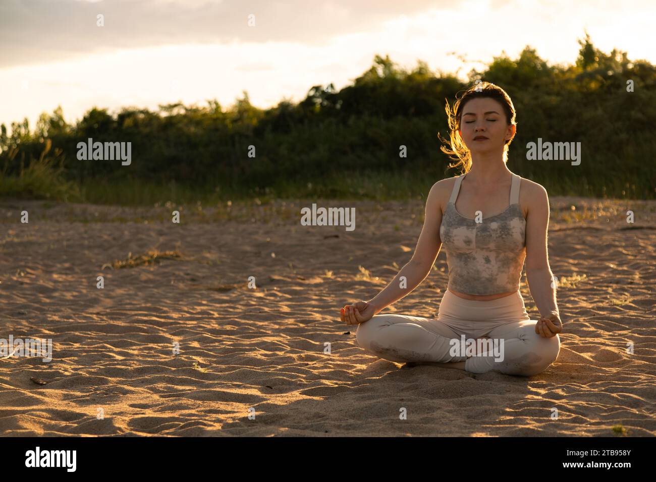 Young beautiful woman practicing yoga outdoors sitting on a lake shore ...