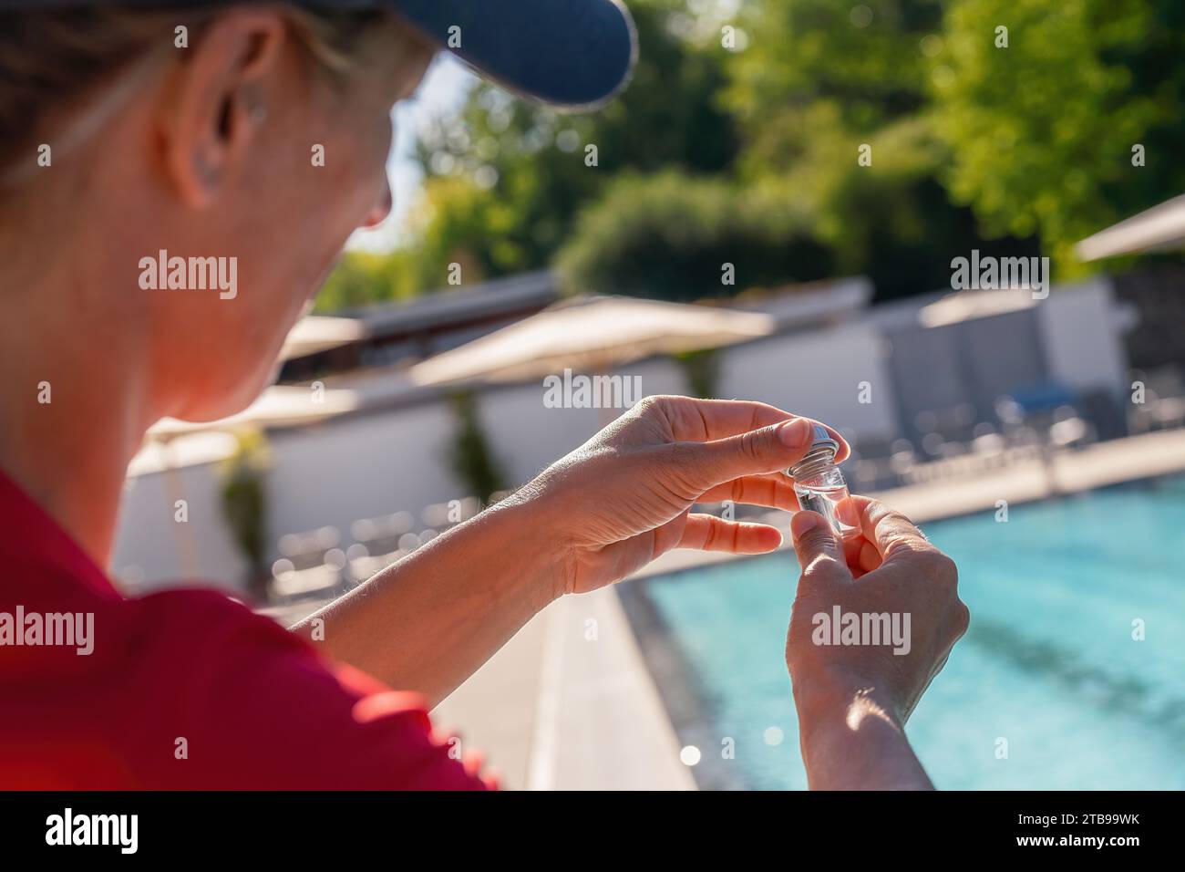 Close-up of woman's hands closing a small vial for PH value test with swimming pool in background Stock Photo