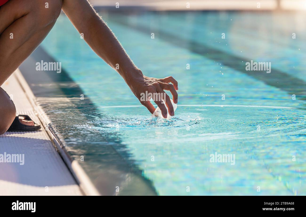 Hand holding a container to collect a water sample from a pool for a pH test Stock Photo