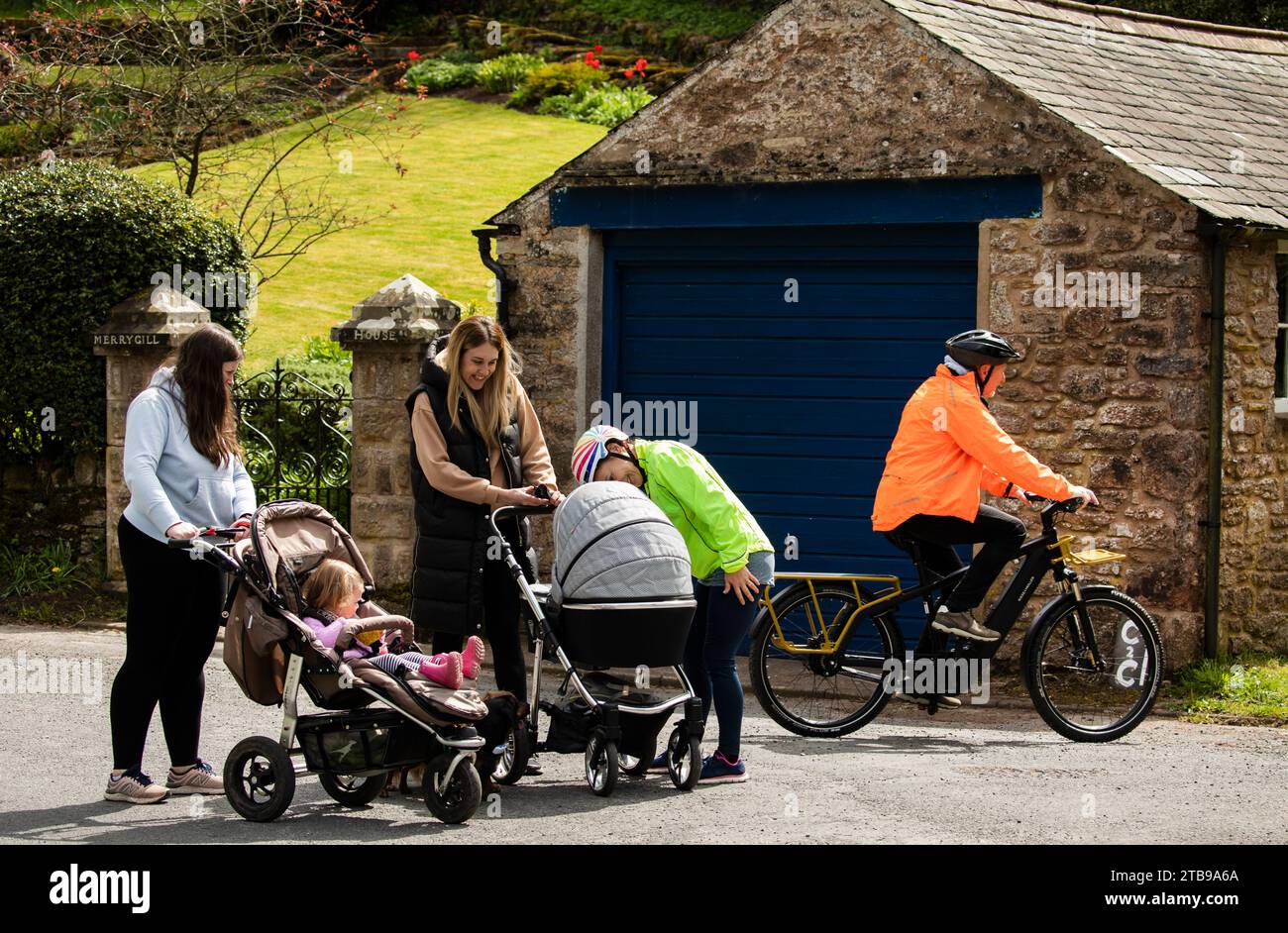 Man and woman cyclists riding electric e bikes and chatting to women with babies in prams in  Hartley. Kirkby Stephen, North Pennines, Cumbria Stock Photo
