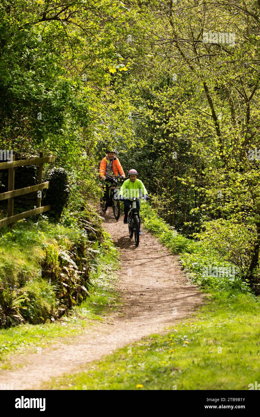 Man and woman cyclists riding electric e bikes off road in a pretty village in springtime, Hartley. Kirkby Stephen, North Pennines, Cumbria Stock Photo